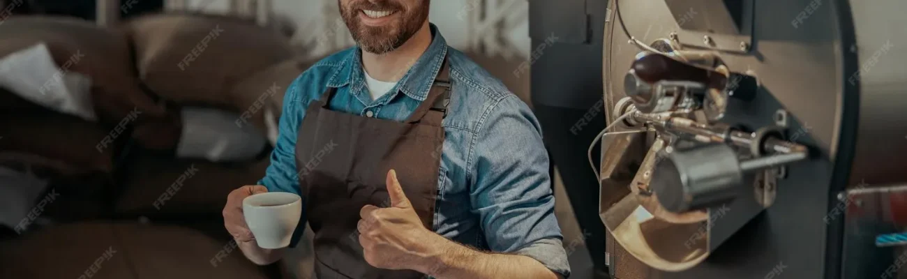 barista-drinking-coffee-sitting-near-coffee-roasting-machine-with-rise-finger-up_386167-18483